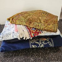 Stack of folded fabrics showing paisley throw, striped textile, navy piece and part of toile fabric