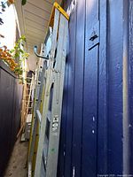 Both ladders leaning against blue wall: yellow fiberglass extension ladder and silver aluminum step ladder