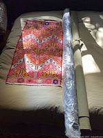 Rug laid out next to two fabric rolls, one roll wrapped in plastic