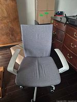 Front view of light gray fabric office chair with white armrests and caster base