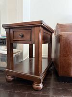 Front and side view of wooden end table showing drawer, shelf, bun feet
