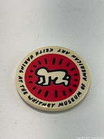 Front view of round Keith Haring Whitney Museum button showing crawling baby icon and surrounding text
