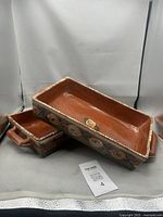two rectangular redware dishes stacked, showing exterior spiral motifs and handles