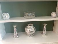 Entire lot displayed on shelving: two crystal clocks, crystal bowl, floral vase, two floral candlesticks