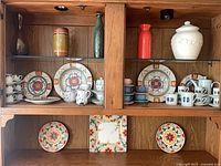 Cabinet view showing floral plates, geometric mugs, pastel cups, vases and canister