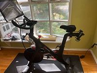 Side view Peloton bike on mat, shoes visible on windowsill