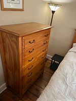 Full front view of tall wooden dresser showing six drawers and brass-tone handles