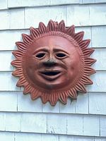 Front view of terracotta sun face plaque mounted on shingled wall