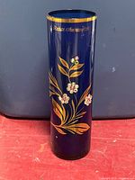 Full view showing cylindrical cobalt blue vase with gold floral design