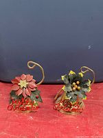 Front view of two brass bells showing poinsettia and holly tops and red “Merry Christmas” lettering