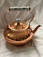 Full view of polished copper kettle showing spout, lid and ceramic handled grip