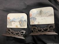 Two painted stone plaques on carved wood stands