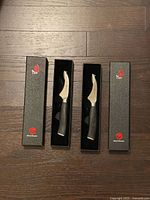 Two curved paring knives in open boxes on wood floor