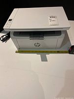 Front view of HP LaserJet M140we printer with power cord and tape measure for scale