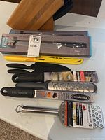 Group shot showing boxed Jamie Oliver knives, loose knives with sheaths, Microplane graters, peeler, and grater plate