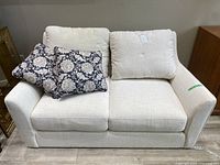 Front view of light beige loveseat with two floral pillows