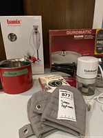 Group shot showing all items: Bamix box, pressure pan, mini chopper, red saucepan, oven mitts, booklets
