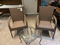 Front view of two woven resin chairs and wrought iron side table