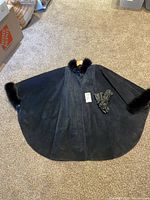 Full view of black suede cape laid flat with gloves on top