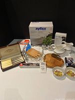 Group shot of all kitchen items including boxed salad spinner, torch, lids, cutlery, serveware