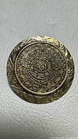 Front view of round sterling silver brooch showing complete Aztec calendar design