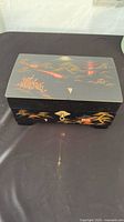 Closed black lacquer jewelry music box showing exterior scenic design and lock