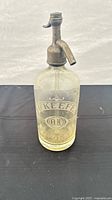 Full view of O'Keefe glass seltzer bottle with metal siphon head