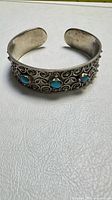 Front view of silver-tone cuff showing filigree and turquoise cabochons