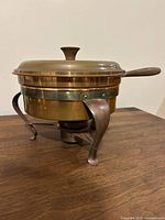 Side view of copper chafing dish on three-leg stand with lid and wood handle