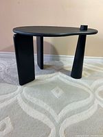 Full view of black kidney-shaped side table showing three distinct legs and top