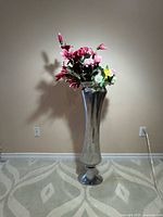 Full view of tall silver aluminum vase standing on carpet