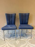 Front view of both blue dining chairs showing upholstery and metal legs