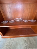 Front view of five clear glass shell bowls on shelf