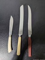 All three knives laid out on dark surface, showing relative size and handle colors