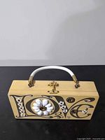 Front angled view showing lettering, cabochon flower, rhinestones, clasp, and handle