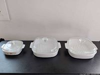 Three square CorningWare casserole dishes with glass lids in graduated sizes