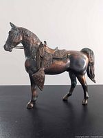 Left side view of cast metal horse showing saddle, reins and overall condition