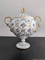 Front view of footed lidded urn showing floral decoration and gilt handles