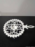 Top view of white cast iron trivet showing openwork and handle