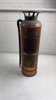 Full view of copper Sodex fire extinguisher standing upright with hose attached