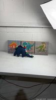 Overall view showing three dinosaur canvas art pieces and blue stegosaurus plush toy