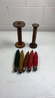 Two large empty wooden bobbins and five smaller thread-wrapped spindles arranged on table