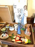 Tray with assorted decor items including mask, puppet parts, floral porcelain, stained glass prism, ceramic cottage and doctor figurine in background