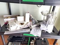 Shelf showing food processor base, bowl, discs, immersion blender and electric slicer