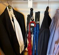 Closet view showing tuxedo jacket, umbrellas, additional suit pieces, striped shirt