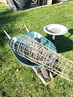 Wheelbarrow holding tomato cages and solar lights beside bird bath