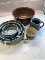 overall view of large brown bowl, nested speckled blue bowls, creamer, sugar