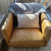 Front view of tan leather armchair with pillow and blanket