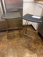 Full view of both black seat gold leg bar stools