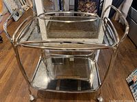 Angled front view showing chrome frame, two mirrored shelves, caster wheels